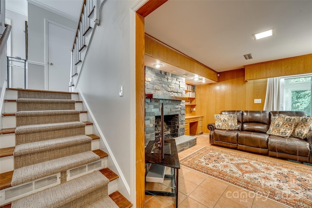 living room featuring a stone fireplace, wooden walls, light tile patterned floors, and ornamental molding