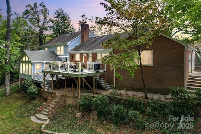 back house at dusk featuring a sunroom and a wooden deck