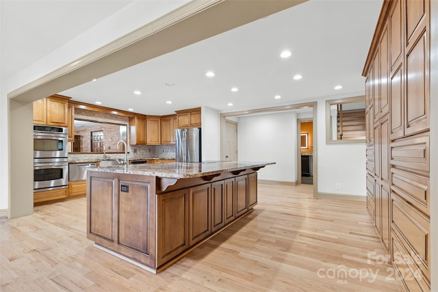 kitchen featuring appliances with stainless steel finishes, light wood-type flooring, light stone counters, and a spacious island