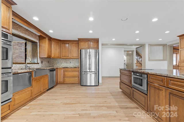 kitchen featuring sink, light stone counters, decorative backsplash, appliances with stainless steel finishes, and light wood-type flooring