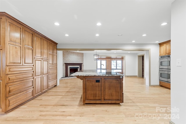 kitchen with a kitchen island with sink, a fireplace, double oven, stone countertops, and light hardwood / wood-style floors