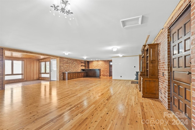 unfurnished living room with a chandelier, brick wall, and light wood-type flooring