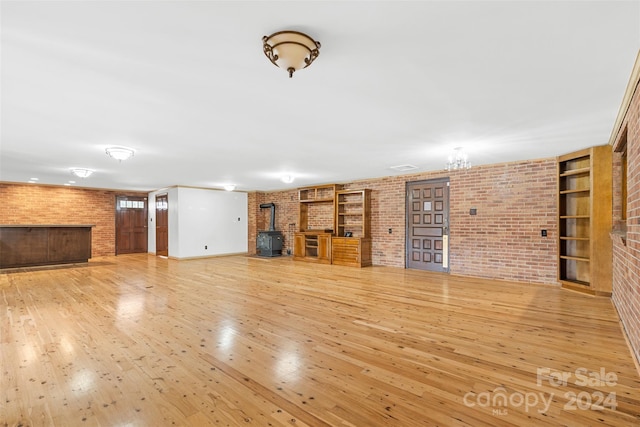 unfurnished living room featuring built in features, a wood stove, brick wall, and light hardwood / wood-style flooring