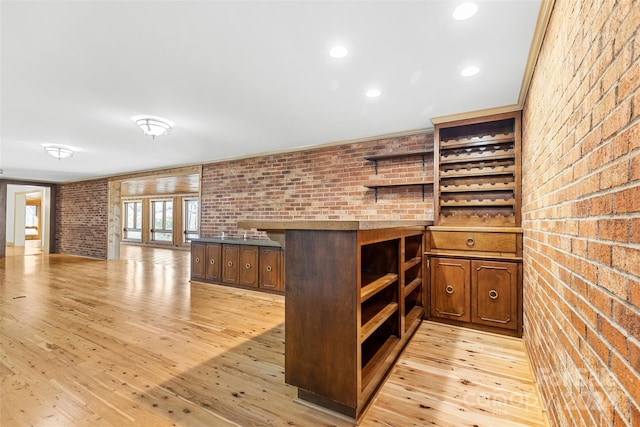 bar with dark brown cabinetry, brick wall, and light hardwood / wood-style flooring