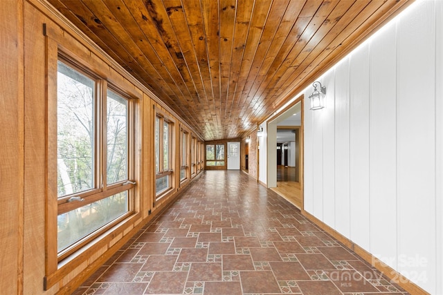 corridor featuring vaulted ceiling, wooden walls, and wood ceiling