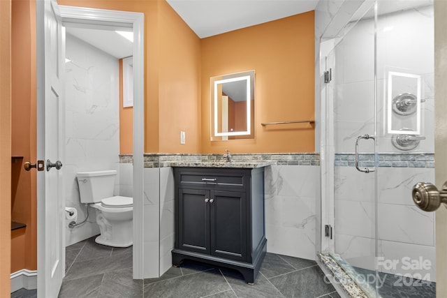 bathroom with vanity, tile patterned floors, toilet, tile walls, and a shower with shower door