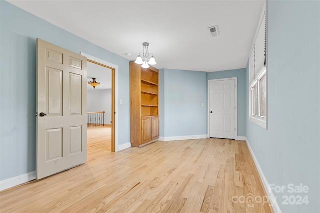 spare room with built in features, light wood-type flooring, and a chandelier