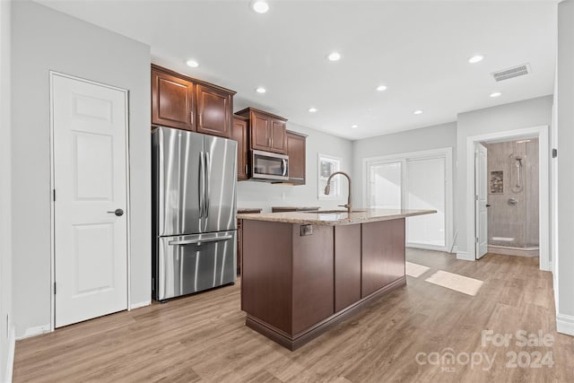 kitchen featuring light stone countertops, appliances with stainless steel finishes, a kitchen island with sink, sink, and light hardwood / wood-style floors