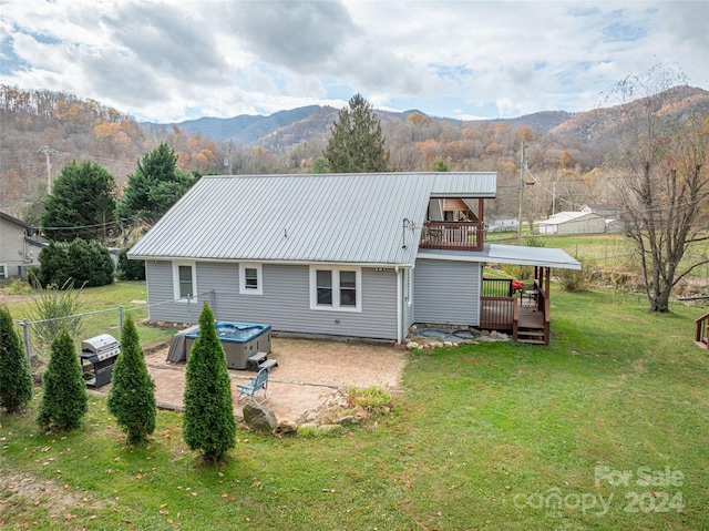 back of house with a mountain view, a yard, a balcony, and a hot tub