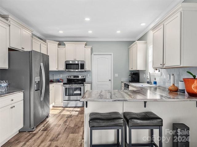 kitchen featuring sink, a kitchen breakfast bar, kitchen peninsula, hardwood / wood-style floors, and appliances with stainless steel finishes