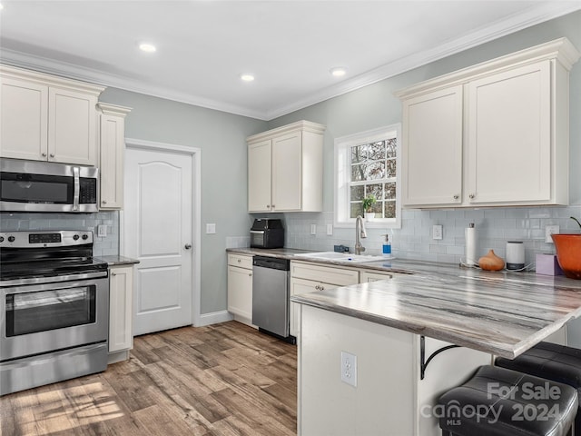 kitchen with sink, stainless steel appliances, light hardwood / wood-style floors, a kitchen bar, and ornamental molding