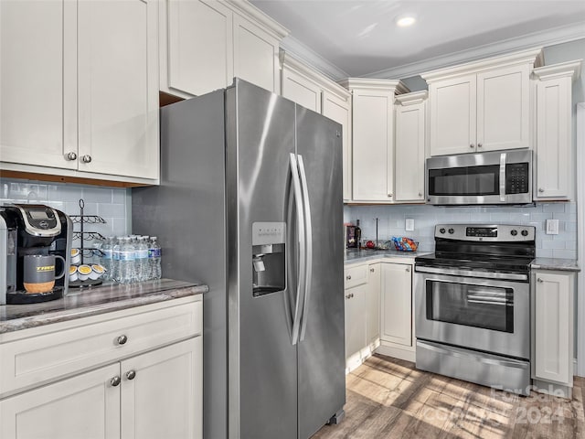 kitchen with backsplash, dark stone counters, crown molding, hardwood / wood-style flooring, and stainless steel appliances