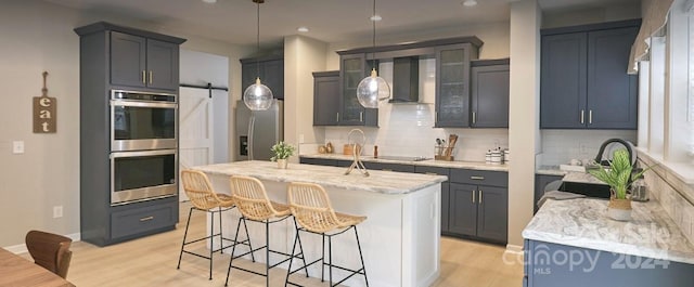 kitchen with a center island, wall chimney range hood, tasteful backsplash, a barn door, and appliances with stainless steel finishes