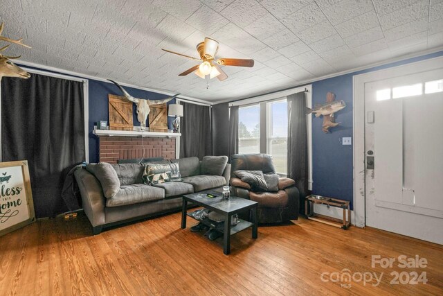 living room featuring hardwood / wood-style flooring, a brick fireplace, ceiling fan, and ornamental molding