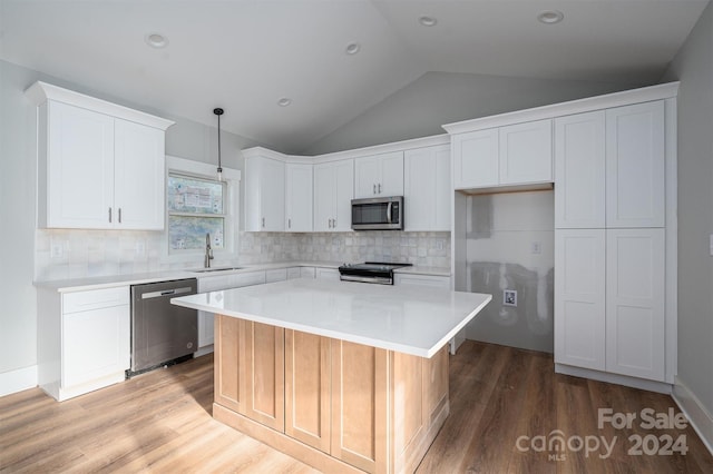 kitchen with appliances with stainless steel finishes, vaulted ceiling, sink, white cabinets, and a center island