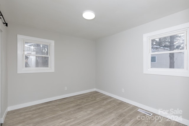 unfurnished room with a barn door and light wood-type flooring