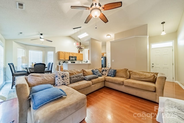 living room with vaulted ceiling, ceiling fan, light hardwood / wood-style floors, and a textured ceiling