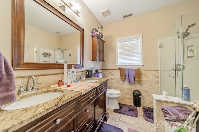 bathroom featuring a shower with door, tile walls, tile patterned flooring, vanity, and toilet