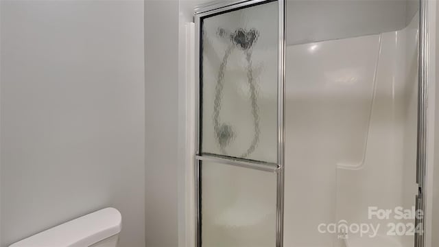 bathroom featuring a shower with door and toilet