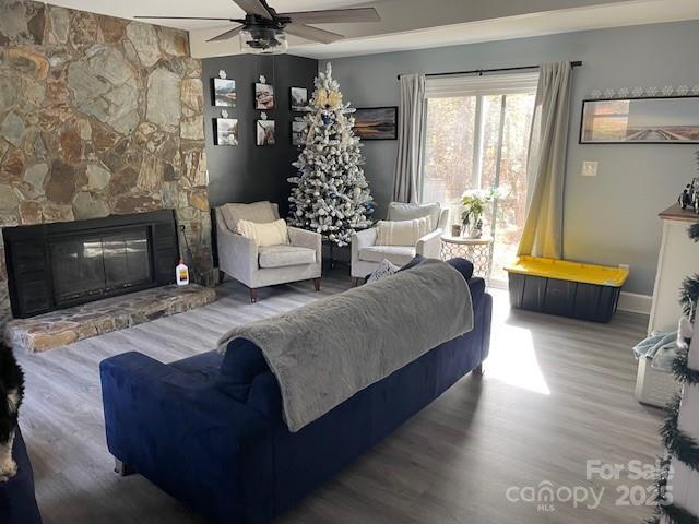 living room with hardwood / wood-style flooring, ceiling fan, and a stone fireplace