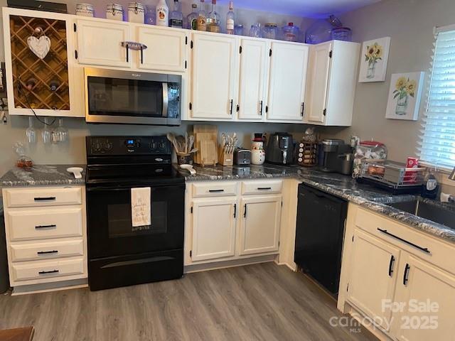 kitchen with dark wood-type flooring, dark stone counters, and black appliances