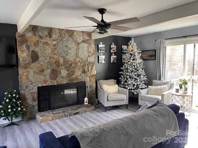 living room featuring hardwood / wood-style floors, a stone fireplace, beamed ceiling, and ceiling fan