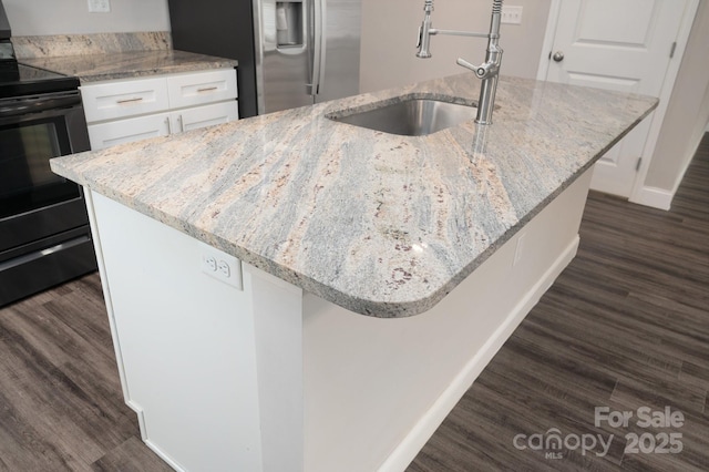 kitchen featuring electric range, stainless steel fridge, white cabinets, and an island with sink