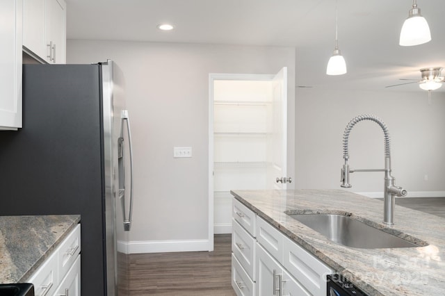 kitchen with stainless steel fridge, light stone counters, white cabinetry, and sink