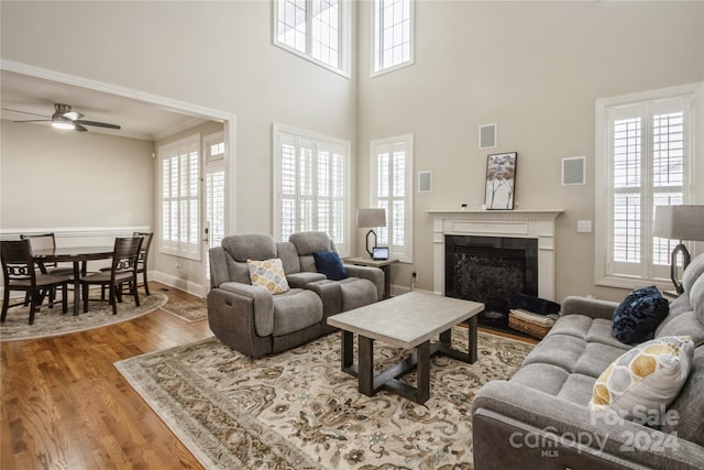 living room with a towering ceiling, ornamental molding, ceiling fan, a fireplace, and hardwood / wood-style floors