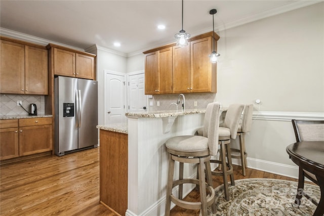 kitchen featuring light stone counters, backsplash, kitchen peninsula, stainless steel fridge, and decorative light fixtures