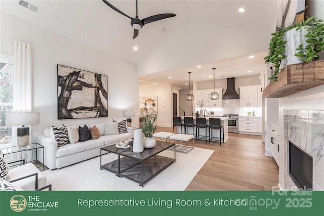 living room featuring ceiling fan, light hardwood / wood-style flooring, a premium fireplace, and lofted ceiling