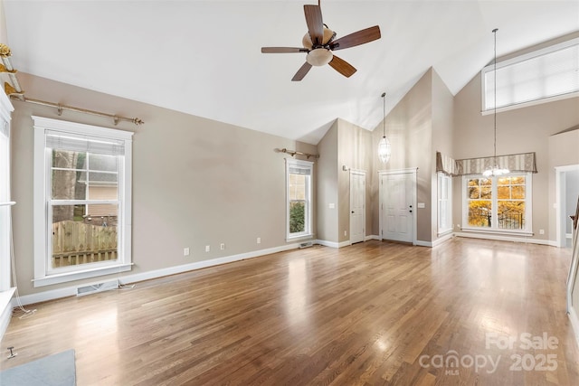 unfurnished living room featuring baseboards, visible vents, wood finished floors, high vaulted ceiling, and ceiling fan with notable chandelier