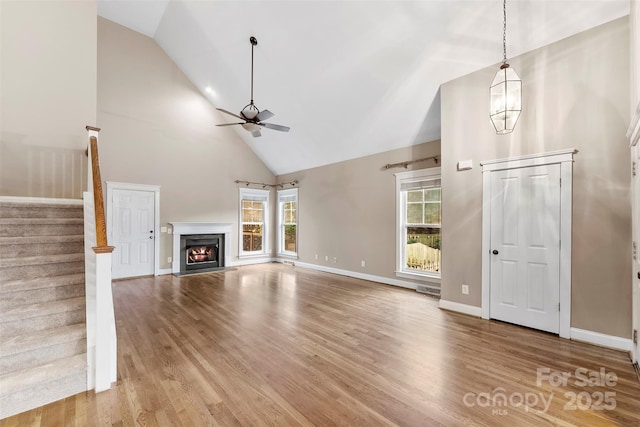 unfurnished living room featuring stairs, a fireplace, wood finished floors, and a ceiling fan