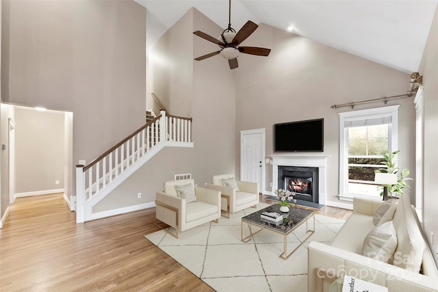 living room with wood finished floors, a ceiling fan, baseboards, stairs, and a glass covered fireplace