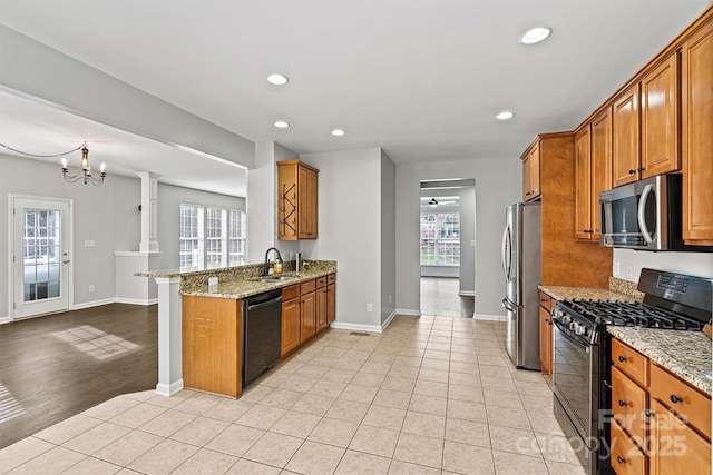 kitchen featuring kitchen peninsula, a healthy amount of sunlight, black appliances, light stone counters, and sink