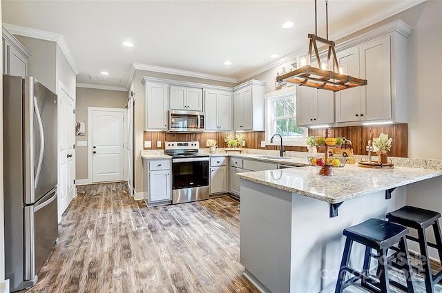 kitchen featuring appliances with stainless steel finishes, light wood-type flooring, light stone counters, sink, and hanging light fixtures