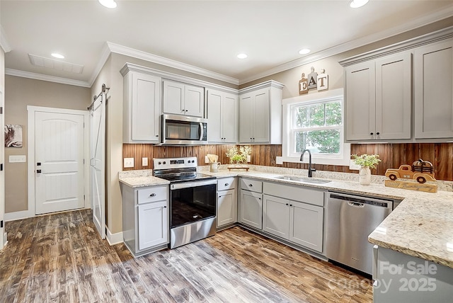 kitchen with gray cabinetry, sink, a barn door, light stone countertops, and stainless steel appliances