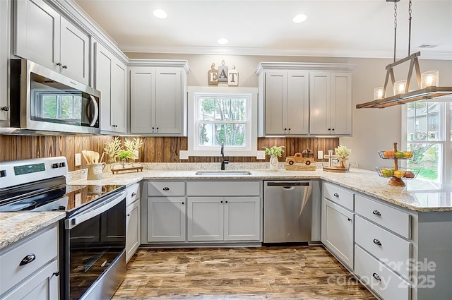 kitchen featuring light stone counters, stainless steel appliances, crown molding, sink, and hanging light fixtures