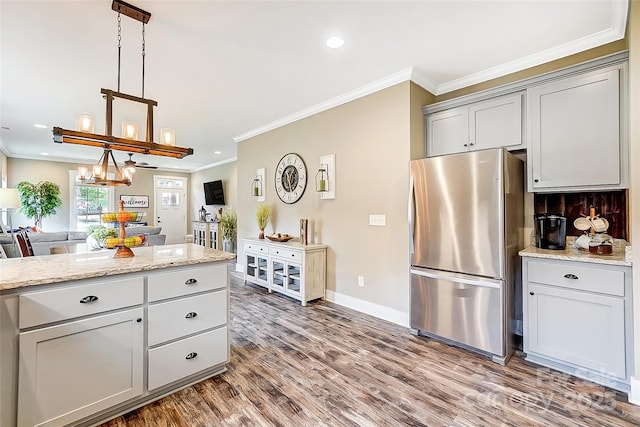 kitchen featuring stainless steel fridge, light stone counters, gray cabinetry, hardwood / wood-style floors, and hanging light fixtures