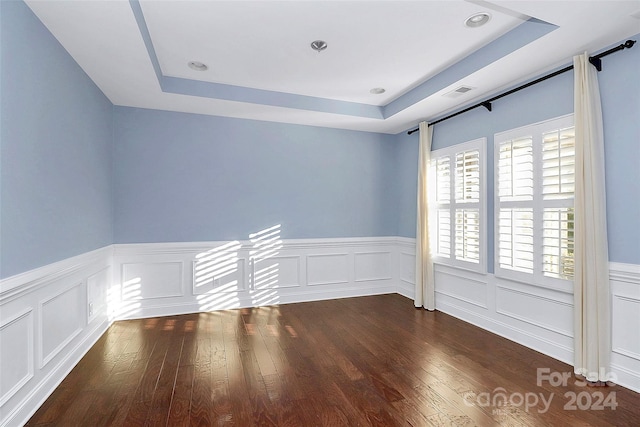 empty room with dark hardwood / wood-style flooring and a tray ceiling