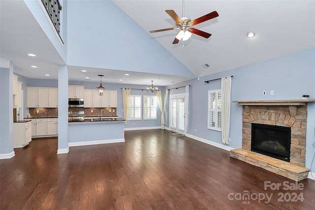 unfurnished living room featuring sink, dark hardwood / wood-style flooring, high vaulted ceiling, a fireplace, and ceiling fan with notable chandelier