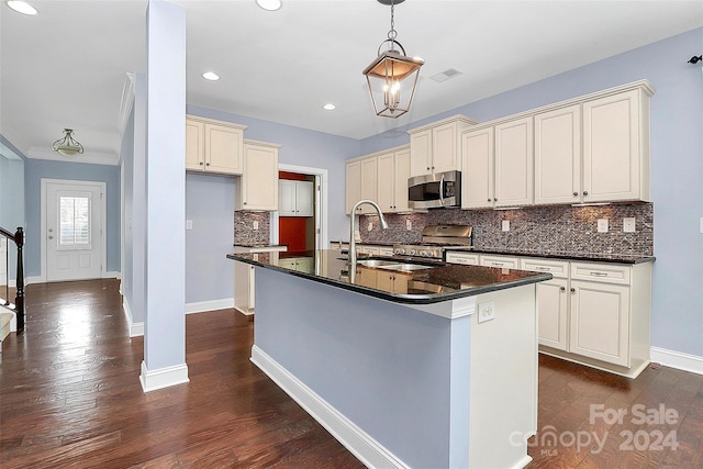 kitchen with sink, dark wood-type flooring, stainless steel appliances, an island with sink, and pendant lighting