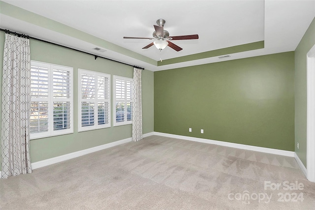 spare room with light colored carpet, a raised ceiling, and ceiling fan