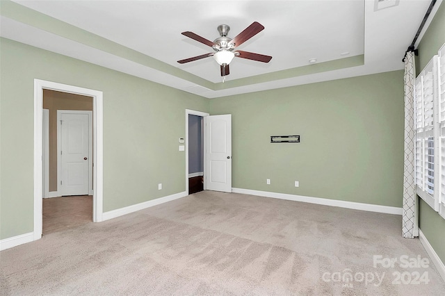 unfurnished bedroom with a raised ceiling, ceiling fan, and light colored carpet