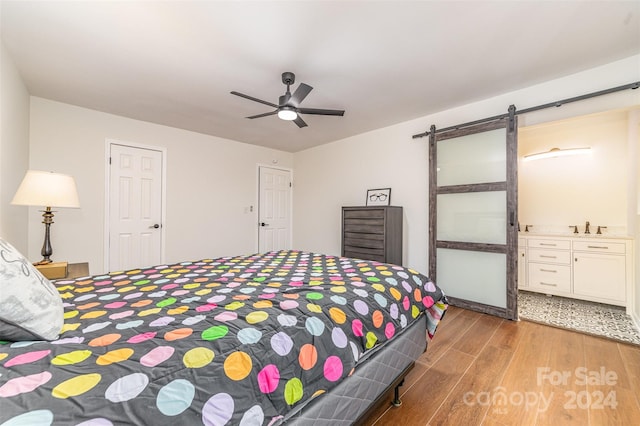 bedroom with a barn door, ceiling fan, and light wood-type flooring