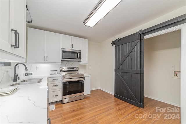 kitchen featuring white cabinetry, sink, stainless steel appliances, a barn door, and light stone counters