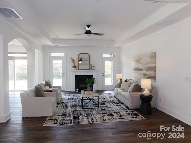 living room with dark wood-type flooring, a raised ceiling, ceiling fan, and a healthy amount of sunlight