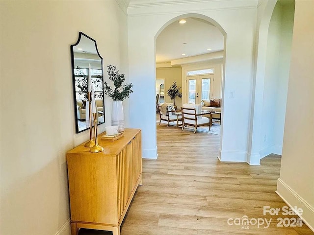 corridor with arched walkways, french doors, baseboards, and light wood finished floors