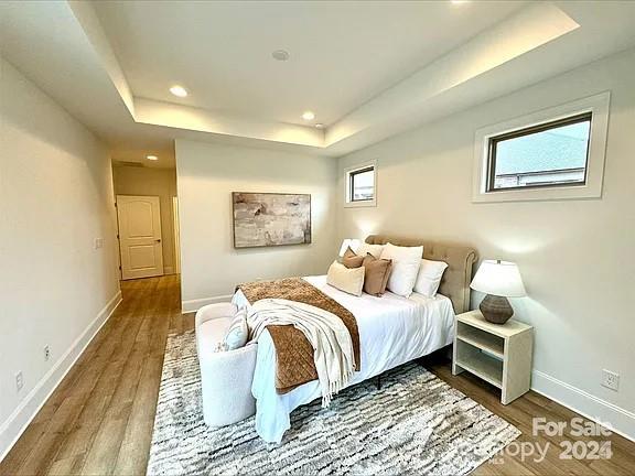 bedroom with baseboards, a raised ceiling, wood finished floors, and recessed lighting