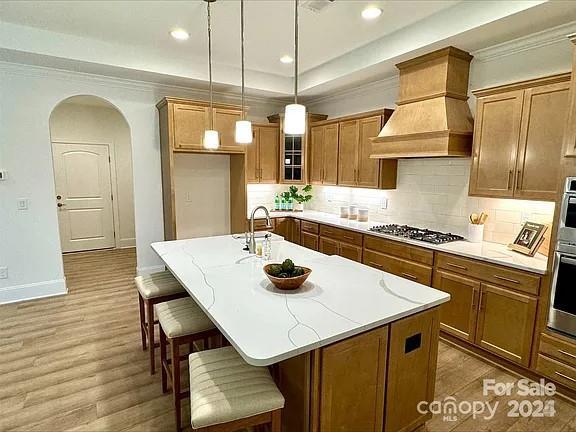 kitchen featuring a center island with sink, arched walkways, brown cabinets, custom exhaust hood, and stainless steel appliances